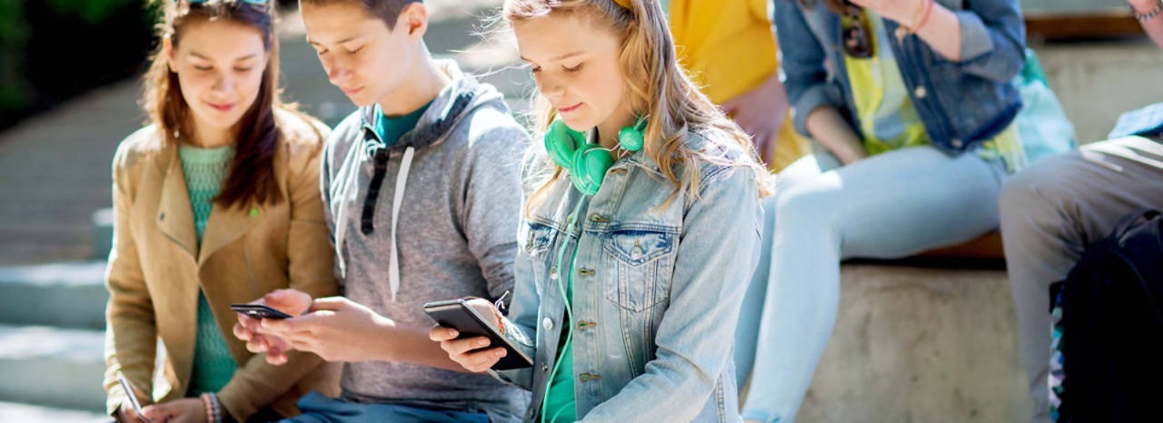 Jugendliche sitzen in einer Gruppe und schauen auf ihr Smartphone