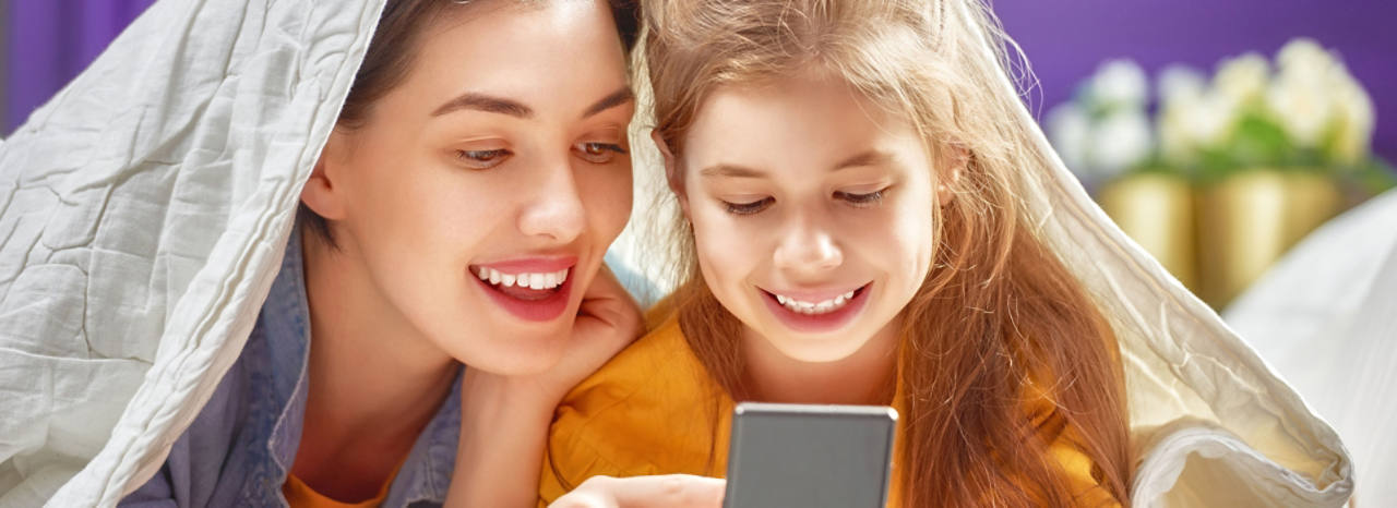 Mutter und Tochter sind unter einer Decke und lachen zusammen am Smartphone