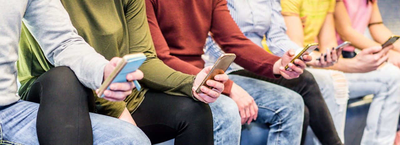 Gruppe von Teenager sitzen auf einer Bank und schauen auf ihr Smartphone