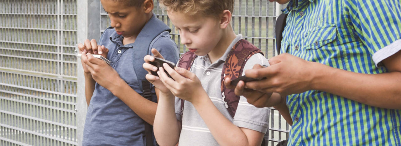 Kinder sitzen zusammen und spielen auf ihren Smartphones