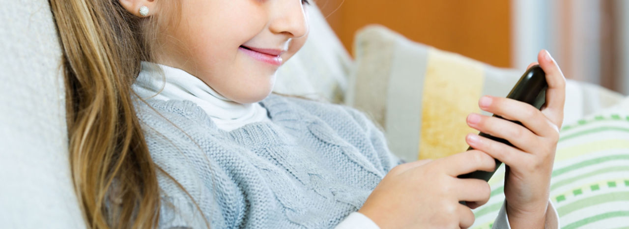 Mädchen sitzt auf dem Sofa und schaut auf ihr Smartphone